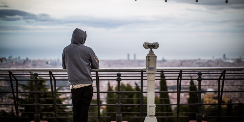 Person and binocular stand, gazing wistfully over Barcelona towards the sea.